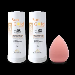 Dois bastões de protetor solar Sun Gold FPS 80 na cor Clara, ao lado de uma esponja de maquiagem rosa em formato de gota